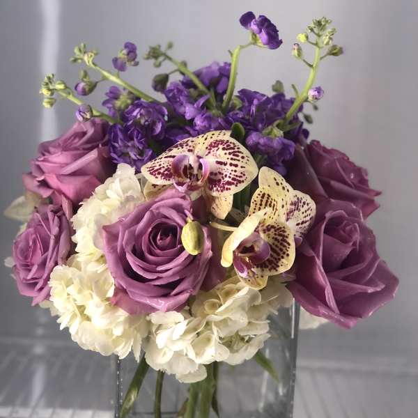 Purple roses and orchids arranged in a clear glass vase