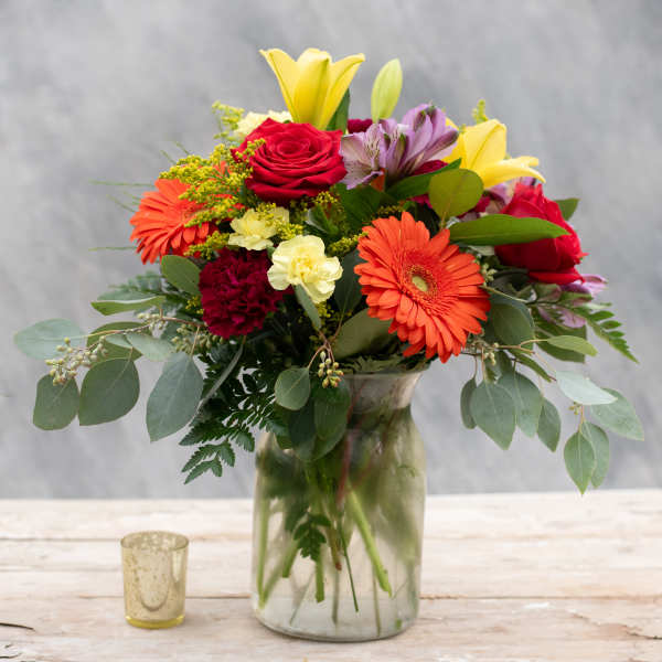 Mixed bouquet of roses, lilies, and gerbera daisies in a glass vase