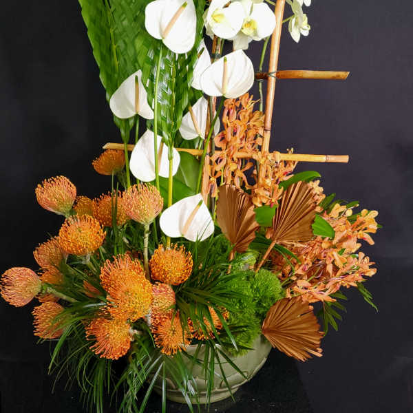 Tropical floral arrangement with white orchids and orange blooms in a low vase