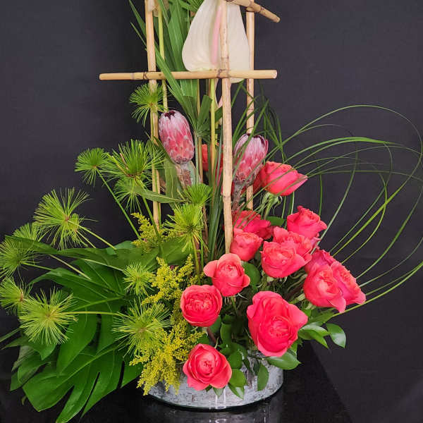 Pink roses and tropical flowers arranged in a bamboo frame with a white vase