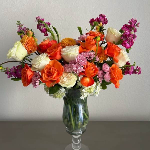Orange and white roses with pink flowers in a glass vase