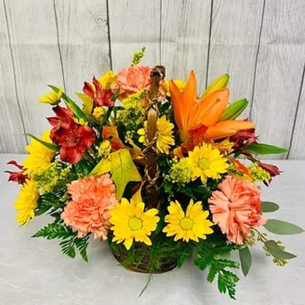 Mixed bouquet with orange lilies, yellow daisies, and peach carnations in a basket