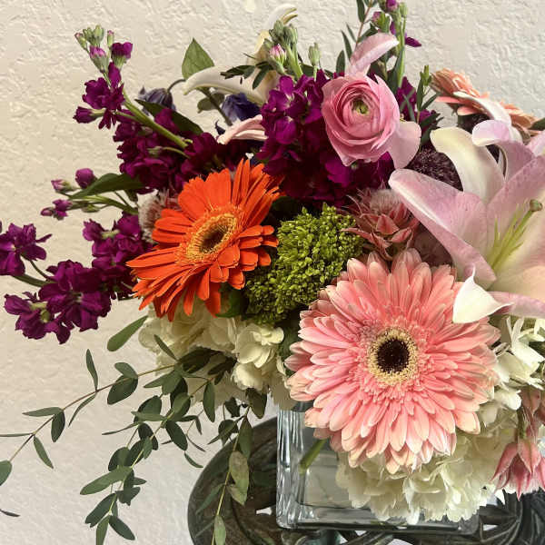 Mixed bouquet with pink lilies, gerbera daisies, and purple blooms in a glass vase