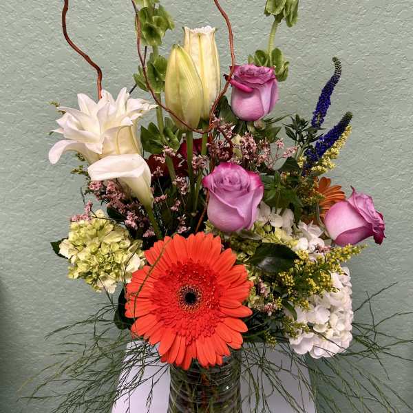 Mixed bouquet with roses, lilies, and a bright gerbera daisy in a glass vase