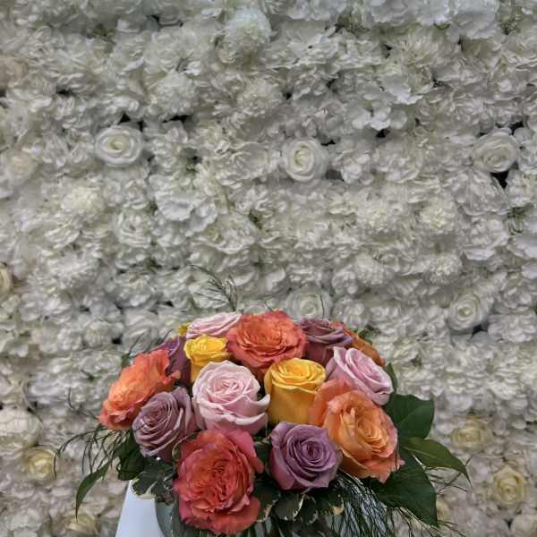 Mixed roses in a glass vase before a white floral wall