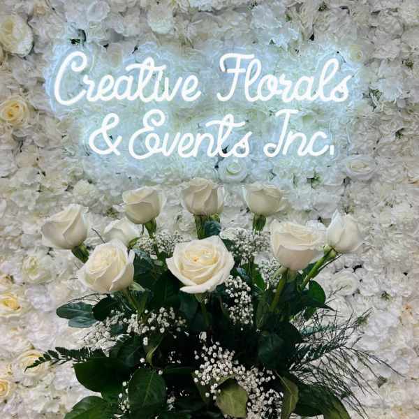 White rose bouquet in a glass vase before a floral wall sign