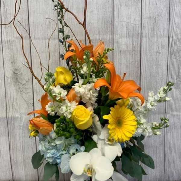 Orange lilies, yellow roses, and white orchids in a glass vase