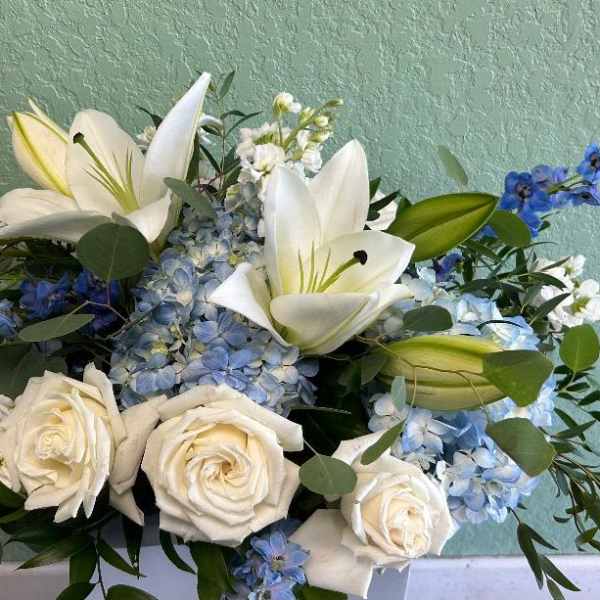 White lilies and roses arranged with blue hydrangeas and small blue flowers