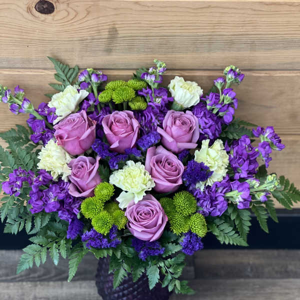 Bouquet of pink roses, purple flowers, and green mums in a dark vase