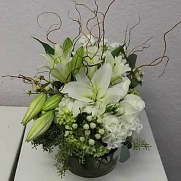 White lily arrangement in a dark round container with curly branches