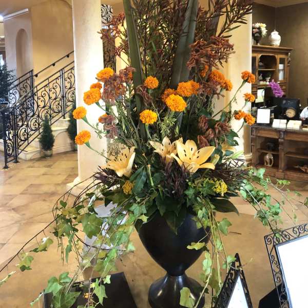 Tall floral arrangement with orange blooms in a black urn vase