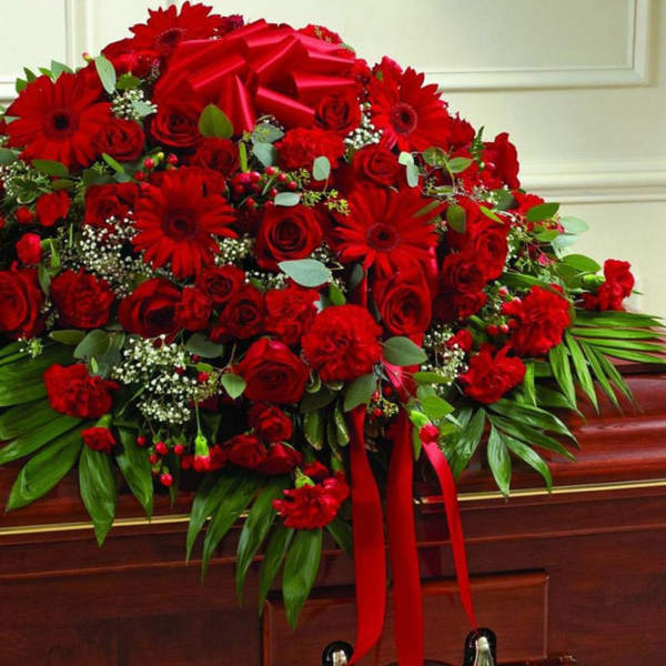 Red casket spray of roses and gerbera daisies with large greenery and a red bow