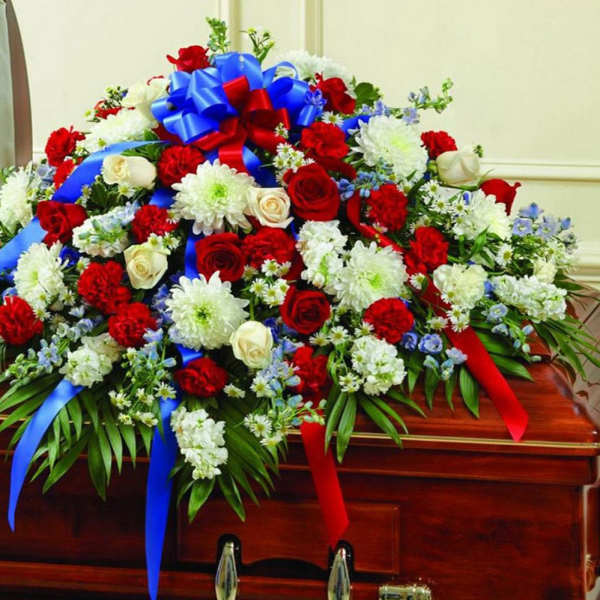 Patriotic red, white, and blue casket spray with roses, carnations, mums and ribbons on a wooden casket