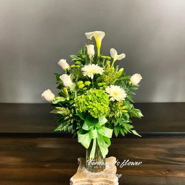 Tall white and green flower arrangement with roses, calla lilies, and hydrangea in a glass vase