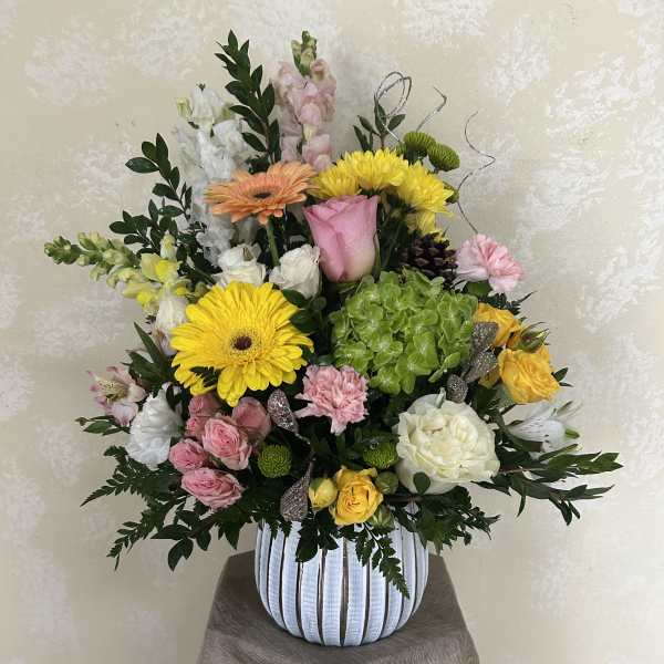 Mixed bouquet in a striped vase with yellow, pink, white, and peach blooms