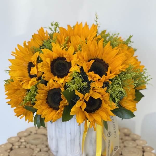 Bouquet of sunflowers in a white vase with a yellow ribbon