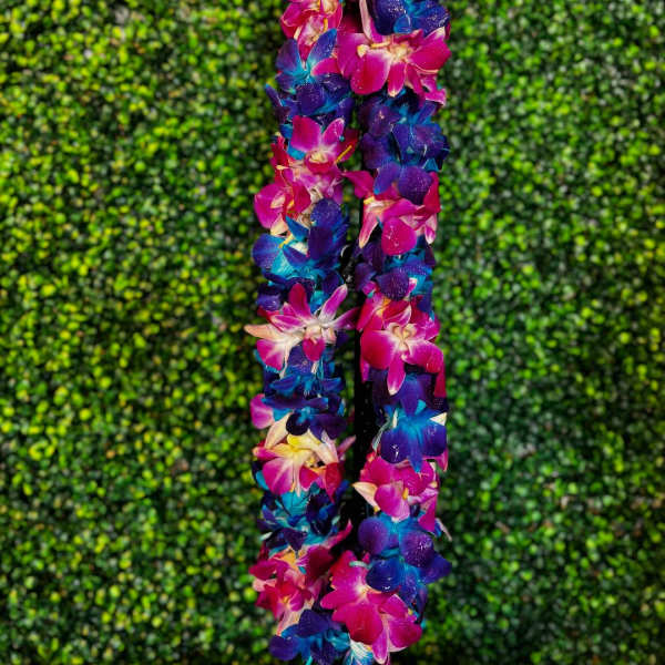Two orchid leis in bright pink, blue, and purple against a green hedge