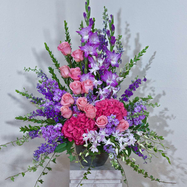 Tall arrangement of pink roses and purple flowers in a dark vase