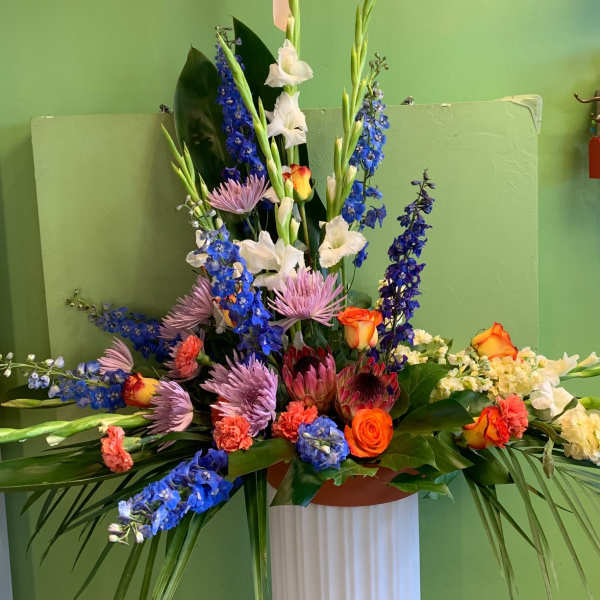 Tall mixed floral arrangement with blue, white, pink, and orange blooms