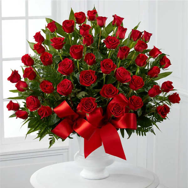 Large arrangement of red roses in a white pedestal vase with red satin bow