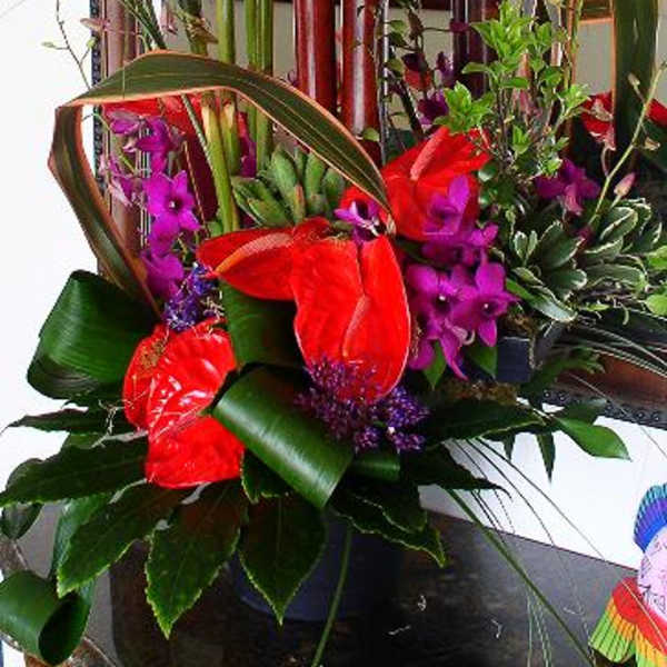 Tropical floral arrangement with red and purple blooms in a dark vase