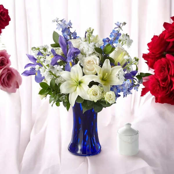 White lilies and roses with blue irises in a cobalt blue vase on a light pink cloth