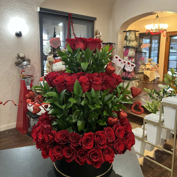 Tiered arrangement of red roses with heart decorations in a black round box