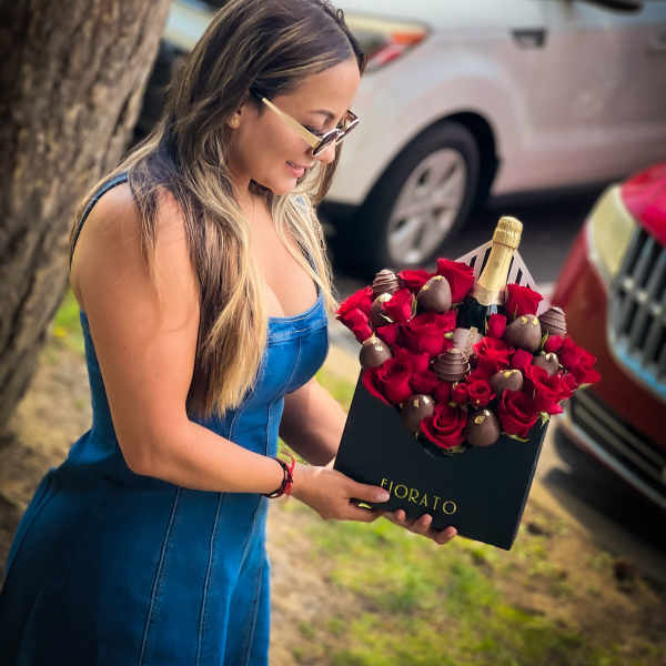 Woman holding a box of red roses and chocolates with a champagne bottle
