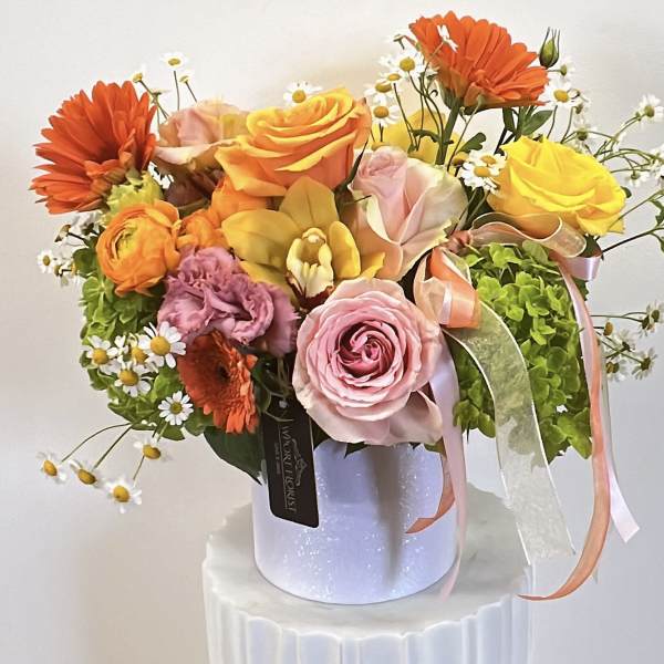 Bouquet of roses, gerbera daisies, and small white daisies in a white hatbox