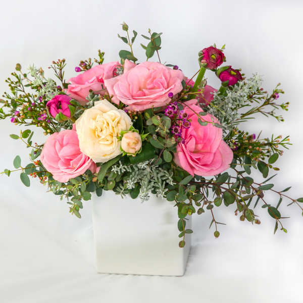 Pink and cream roses arranged in a white square vase