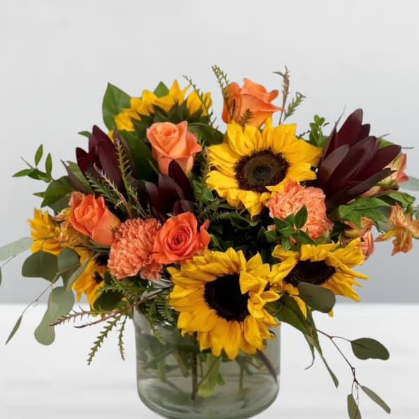 Bouquet of sunflowers, orange roses, and carnations in a glass vase