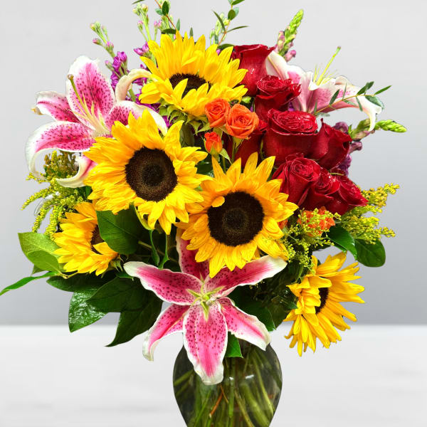 Bouquet of sunflowers, red roses, and pink lilies in a glass vase