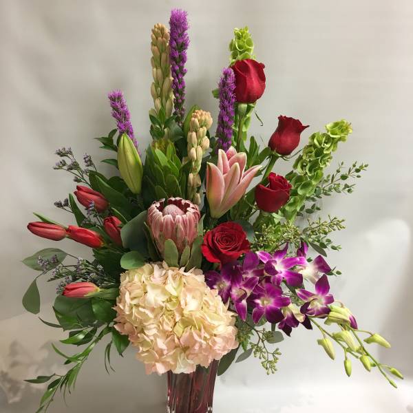 Mixed bouquet with roses, lilies, hydrangea, and orchids in a glass vase