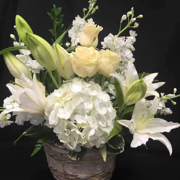 White lilies and pale roses in a woven basket with a large white hydrangea bloom