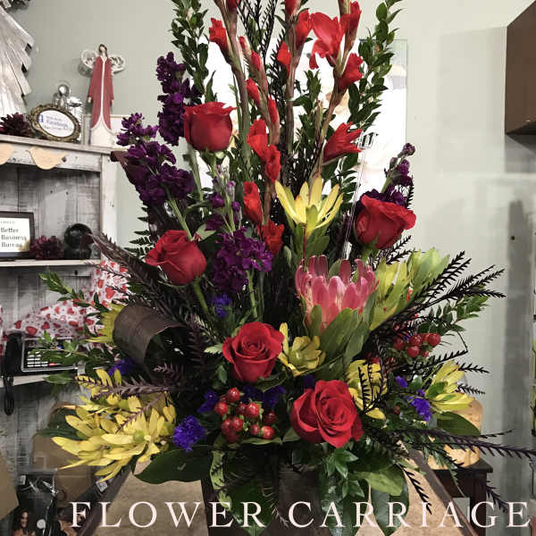 Tall mixed floral arrangement with red roses, purple blooms, and yellow flowers in a dark container