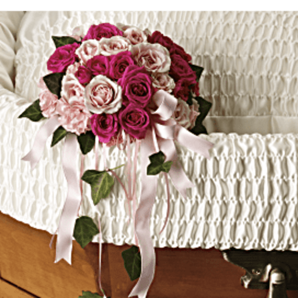 Pink and white rose bouquet with ribbon draped over a white casket