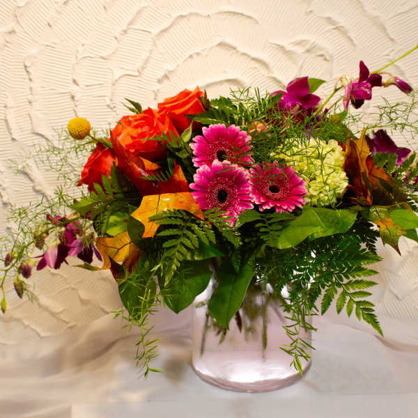 Mixed bouquet of orange roses, pink gerberas, and purple orchids in a glass vase