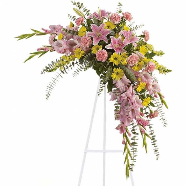 Standing spray of pink lilies, pink carnations, and yellow daisies on a white easel