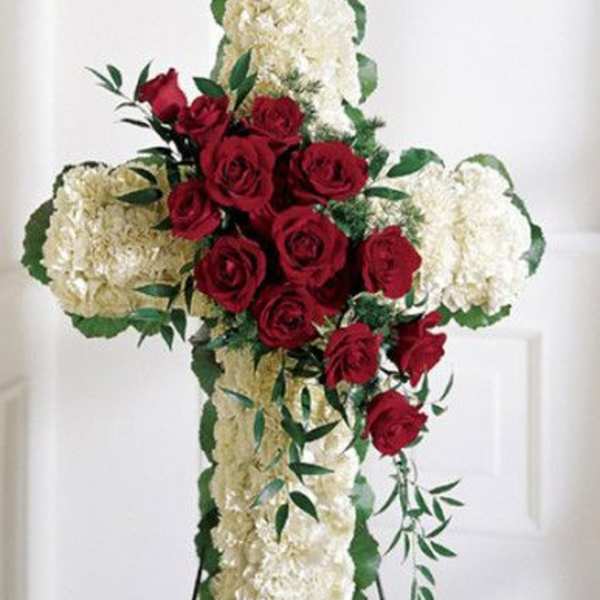 Standing white floral cross with red roses at the center on a metal easel.