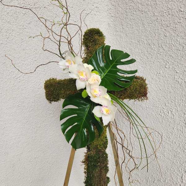 Moss-covered cross arrangement with white orchids and large tropical leaves