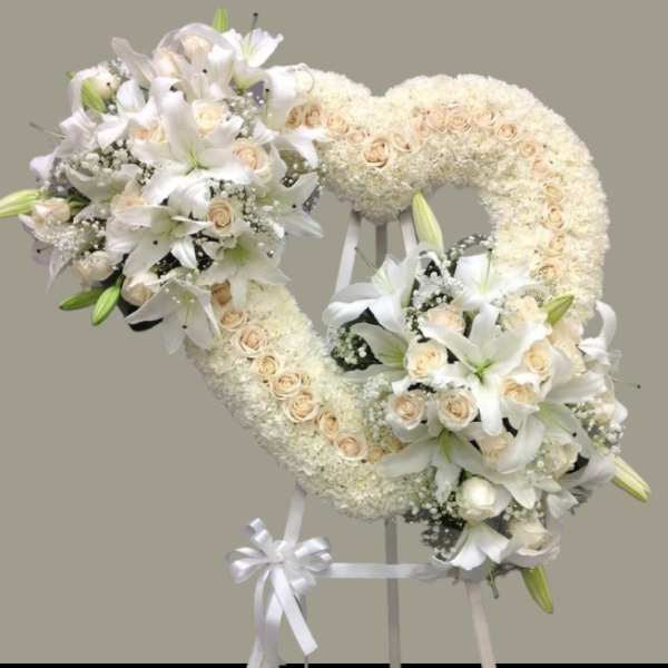 Heart-shaped white floral wreath on a stand with ribbon