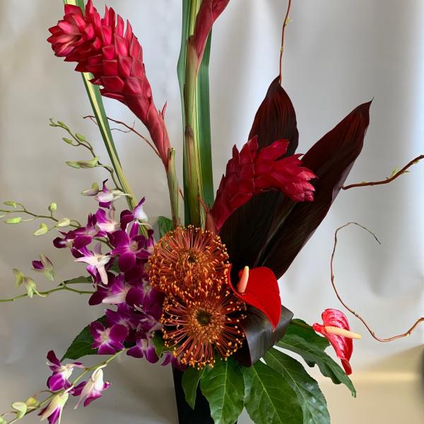 Tropical floral arrangement with red ginger, purple orchids, and anthuriums in a black vase