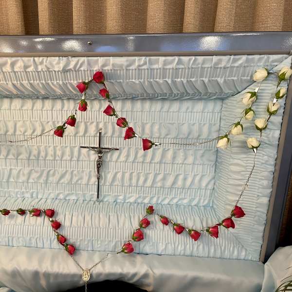 Red and white rosebud rosary draped inside a light blue open casket interior