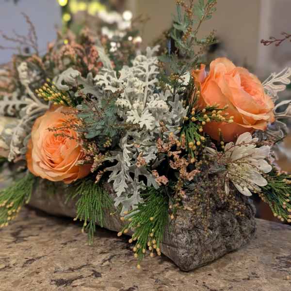 Low rustic arrangement with peach roses, cream blooms, and textured evergreen foliage in a bark-like container