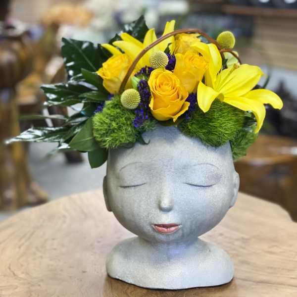 Yellow roses and lilies arranged in a gray sculpted head vase
