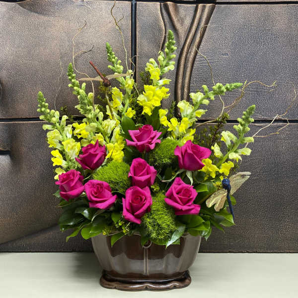 Pink roses and yellow snapdragons arranged in a brown vase.