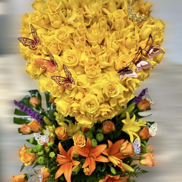 Tall arrangement with a yellow rose heart over orange lilies and roses with butterfly accents