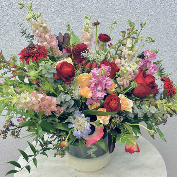 Large mixed bouquet in a round vase with red, pink, peach, and white flowers