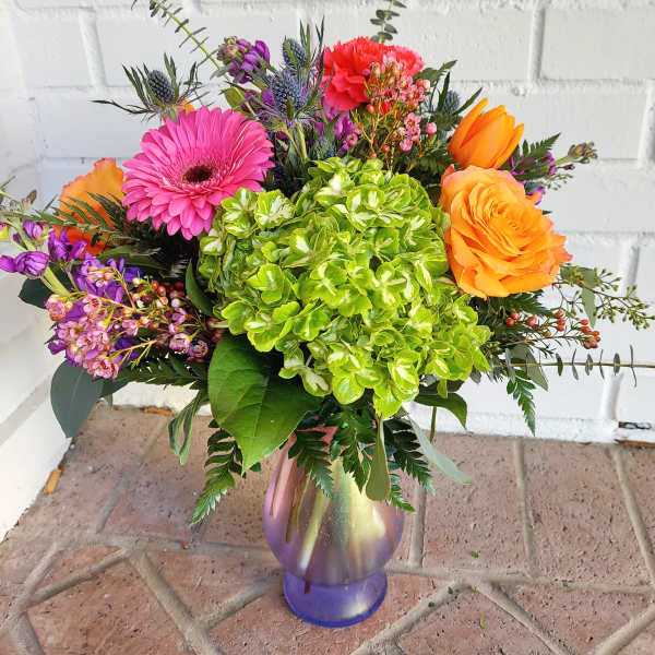 Colorful bouquet with hydrangea, gerbera daisy, roses, and tulips in a glass vase.