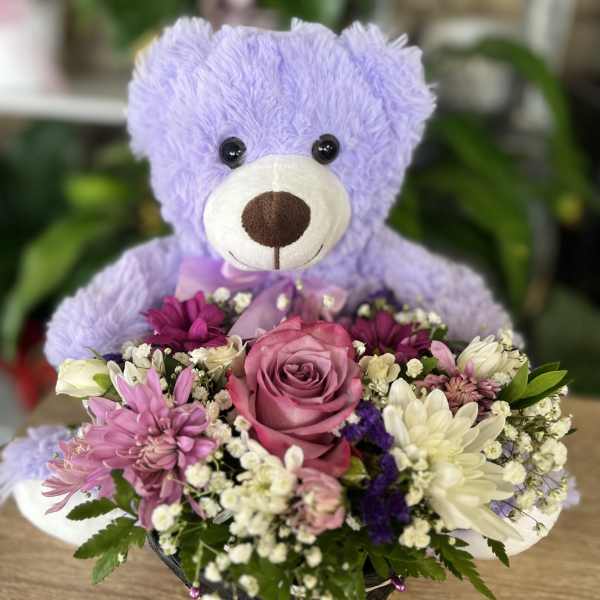 Lavender teddy bear holding a mixed flower basket with a pink rose